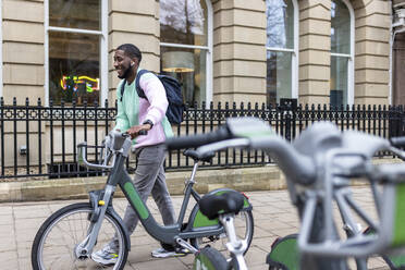 Happy man with electric bicycle walking on footpath - WPEF05889