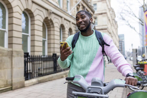 Mann steht mit Elektrofahrrad und hält Smartphone - WPEF05890