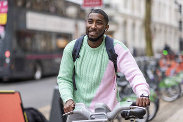 Lächelnder Mann mit Elektrofahrrad zu Fuß in der Stadt - WPEF05891