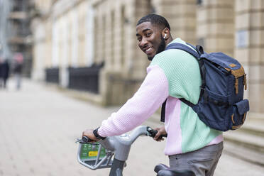 Smiling man with backpack wheeling electric bicycle - WPEF05893