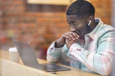 Worried freelancer looking at laptop sitting in cafe seen through glass - WPEF05900