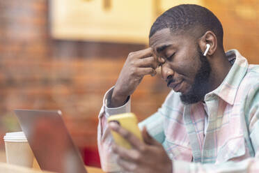 Freiberufler mit Laptop und Smartphone im Café sitzend durch Glas gesehen - WPEF05902