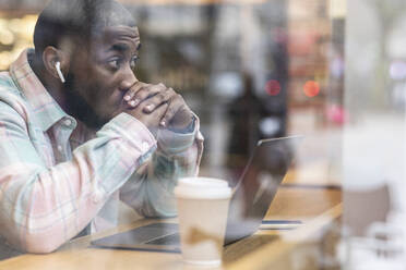 Worried freelancer with laptop sitting at cafe seen through glass - WPEF05905