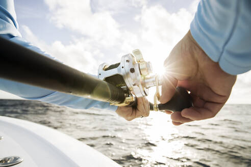 Close up shot of mans Hände reeling in Angelrute mit sunburst - CAVF95820