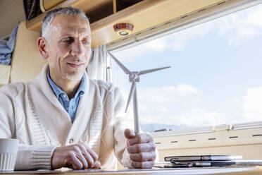 Mann hält Modell einer Windkraftanlage neben dem Fenster eines Wohnmobils - EIF03535