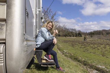 Woman having coffee sitting on doorstep of motor home - EIF03540