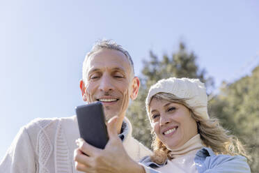 Smiling mature couple taking selfie over smart phone on sunny day - EIF03546