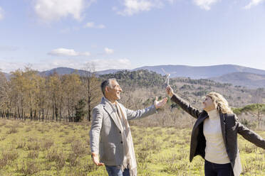 Cheerful mature couple with wind turbine model dancing on weekend - EIF03558