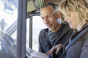 Mature couple looking at map and talking inside camper van on weekend travel - EIF03577