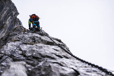 Mann klettert auf felsigem Berg Klettersteig - MCVF00958