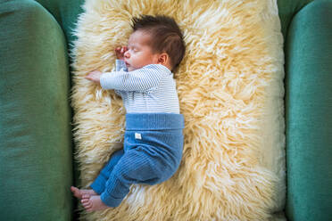 Hochformatige Ansicht eines neugeborenen Babys, das auf einer Schafsfelldecke liegt. - CAVF95824