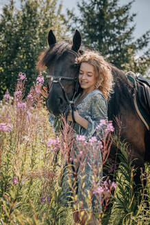Frau in Wildblumen im Gespräch mit einem Pferd. - CAVF95839