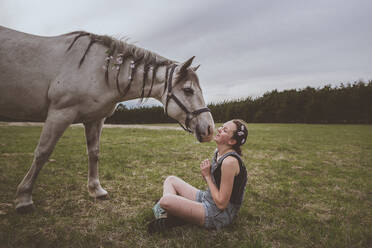 Ein Teenager-Mädchen sitzt mit grauem Pferd mit Zöpfen und Blumen - CAVF95841