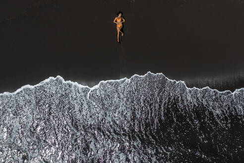 Frau liegt in ihrem Bikini an einem schwarzen Sandstrand in Hawaii - CAVF95855