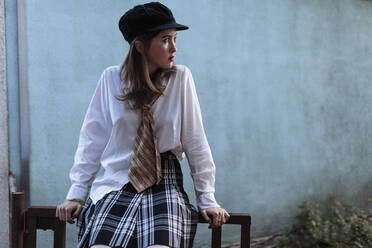 A woman sits on a fence in a plaid skirt on her head a cap - CAVF95857