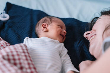 Newborn baby lying in bed and smiling next to his mother. - CAVF95863