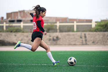 Junge Fußballspielerin kickt den Ball auf dem Spielfeld - CAVF95903