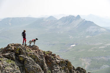 Frau betrachtet die Berge beim Wandern mit Hund im Urlaub - CAVF95913