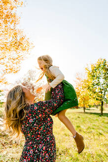 Side view of a mother throwing her daughter into the air - CAVF95916