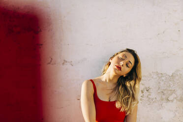 Young woman with head cocked in front of wall - DCRF01065