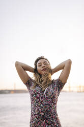 Carefree woman with hands behind head in front of sea - DCRF01073