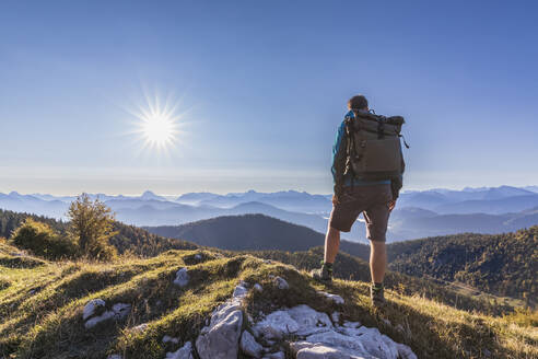 Männlicher Wanderer bewundert die Bayerischen Voralpen bei nebligem Sonnenaufgang - FOF13030