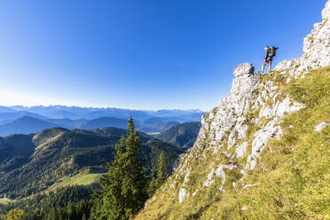 Male hiker admiring forested landscape of Bavarian Prealps from edge of steep mountain ridge - FOF13041