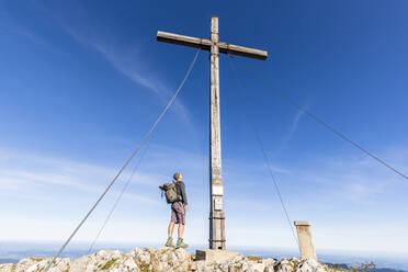 Männlicher Wanderer unter dem Gipfelkreuz auf der Benediktenwand stehend - FOF13043