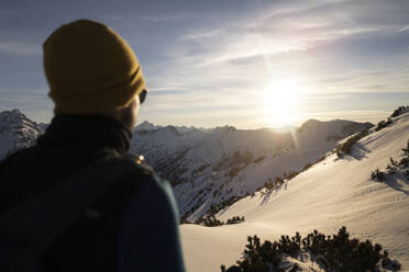 Man wearing knit hat enjoying sunrise on snowy mountain - MALF00393