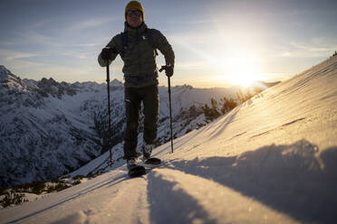 Man with ski pole walking on snowcapped mountain at sunrise - MALF00398