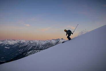 Mann beim Skifahren auf einem schneebedeckten Berg bei Sonnenuntergang - MALF00399