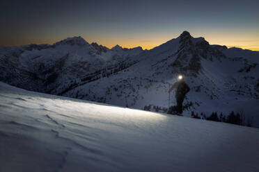 Mann mit Stirnlampe auf verschneitem Berg bei Sonnenuntergang - MALF00400