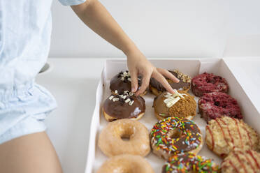 Hand eines Mädchens mit Schokoladenbelag auf Krapfen in einer Schachtel - SVKF00043