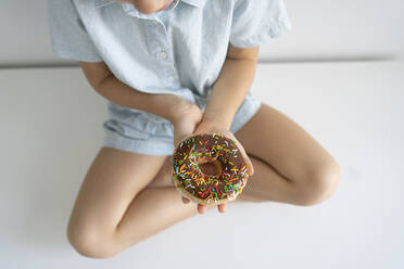 Girl with doughnut sitting cross-legged on table - SVKF00046