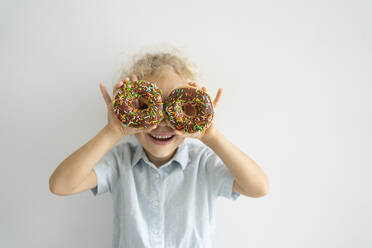 Happy girl covering eyes with doughnuts standing in front of wall - SVKF00047