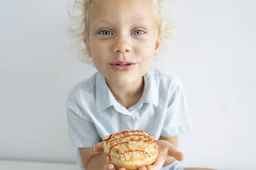 Girl holding doughnut sitting in front of wall - SVKF00053