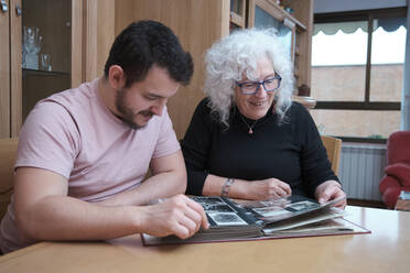 Smiling mother and her adult son look at old photos together. - CAVF95936