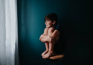 Ein fröhlicher Junge sitzt auf einem Hocker vor einer dunkelblauen Wand. - CAVF95945