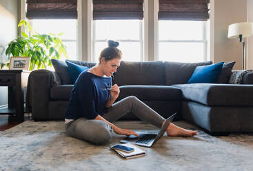 Woman sitting on floor in living room working on computer. - CAVF95947