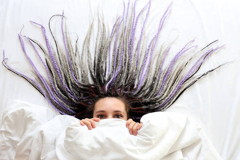 Young women with dreadlocks is peeping out under the blanket - CAVF95965