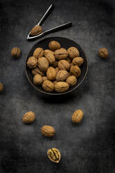 Studio shot of nutcracker and bowl of walnuts lying against black background - LVF09213