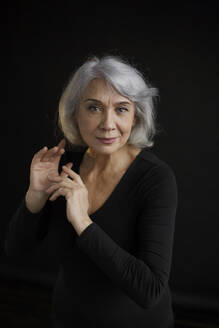 Smiling senior woman with gray hair against black background - LLUF00472
