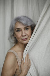 Senior gray haired woman by curtain at home - LLUF00486
