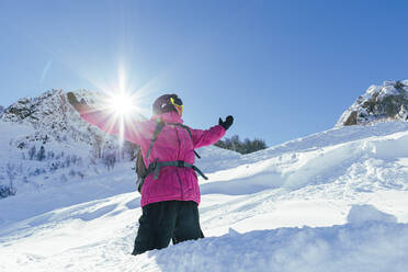 Mann steht mit ausgestreckten Armen auf einem verschneiten Berg an einem sonnigen Tag - OMIF00750