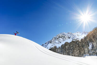 Mann hält Snowboard stehend mit ausgestreckten Armen an einem sonnigen Tag - OMIF00752
