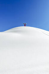 Mann mit Snowboard und erhobenen Armen auf einem schneebedeckten Berg stehend - OMIF00753