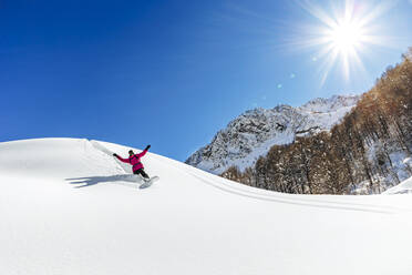 Mann beim Snowboarden auf einem verschneiten Berg an einem sonnigen Tag - OMIF00754