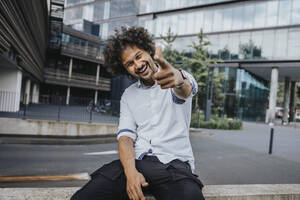Happy young man gesturing in front of modern building - MFF08923