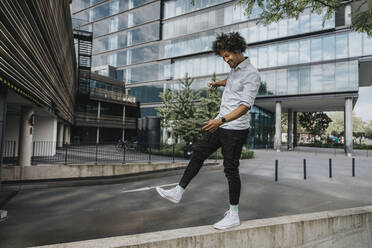 Playful young man balancing on ledge by modern buildings - MFF08929