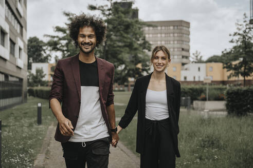 Happy couple holding hands walking on footpath - MFF08937